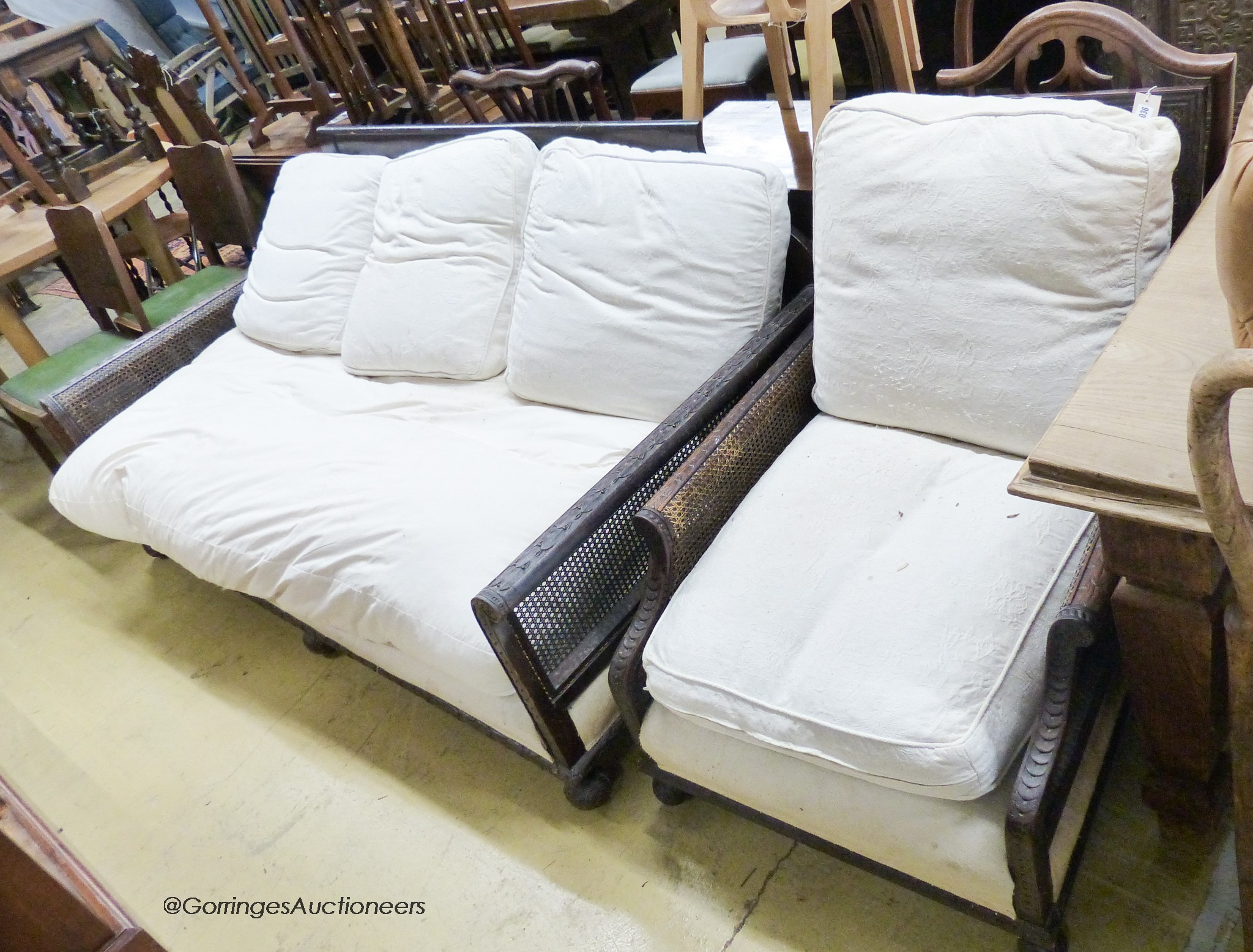 An early 20th century carved mahogany bergere settee, W.186cm D.94cm H.85cm, together with a similar armchair